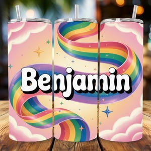 Könnte beinhalten: Ein personalisierter Becher mit dem Namen "Benjamin" in einer kräftigen Retro-Schriftart. Das Design umfasst ein lebendiges Regenbogenband vor einem pastellfarbenen rosa und gelben Hintergrund mit Wolken und Sternen. Der Becher hat einen silbernen Deckel und einen Strohhalm.