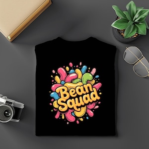 May include: Black t-shirt with a colorful graphic that reads "Bean Squad." The design features cartoon-style beans in various colors, including pink, yellow, blue, and green, arranged in a splash-like pattern.