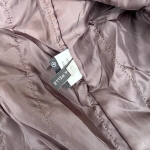 May include: Close-up of a quilted, mauve-colored fabric, possibly the lining of a jacket or coat. The stitching creates a diamond pattern. A label with the text "A PELLE" and size "42" is visible.