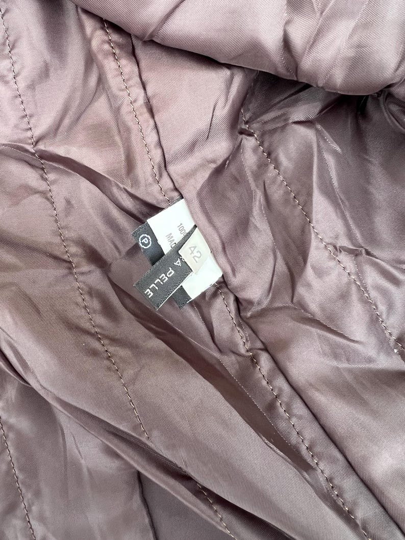 May include: Close-up of a quilted, mauve-colored fabric, possibly the lining of a jacket or coat. The stitching creates a diamond pattern. A label with the text "A PELLE" and size "42" is visible.