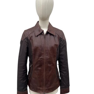 May include: A brown leather jacket with a zip-up front, collar, and side pockets. The jacket has dark brown sleeves and a lighter brown body. The jacket is displayed on a mannequin.