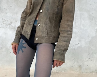 Può includere: Giacca in pelle scamosciata marrone con colletto in ecopelliccia e bottoni. La giacca ha due tasche sul petto. La modella indossa biancheria intima nera e collant blu.