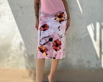 May include: A pale pink halter-neck top and a knee-length skirt. The skirt has a floral design with red and yellow flowers on a pink and white backdrop. The outfit is finished with clear sandals.