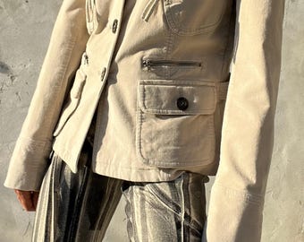 May include: Beige corduroy blazer with multiple pockets and a button closure. The jacket has a classic design with a tailored fit. Paired with black and white striped shorts. The outfit is suitable for casual wear.