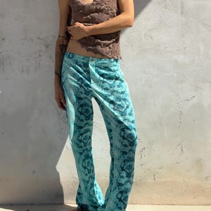 May include: A pair of turquoise and dark blue trousers featuring a snakeskin pattern, paired with a brown textured camisole top. The trousers have a button closure at the waist and a straight-leg fit, while the top has thin spaghetti straps.