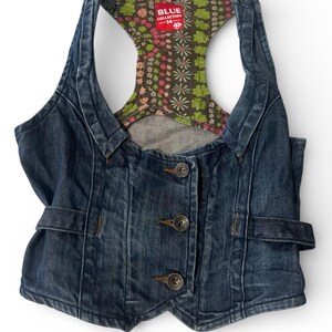 May include: A dark blue denim vest featuring a racerback design with a multi-colored floral pattern lining. The front includes three metal buttons and side adjustment tabs. A red label at the neckline reads BLUE COLLECTION M.
