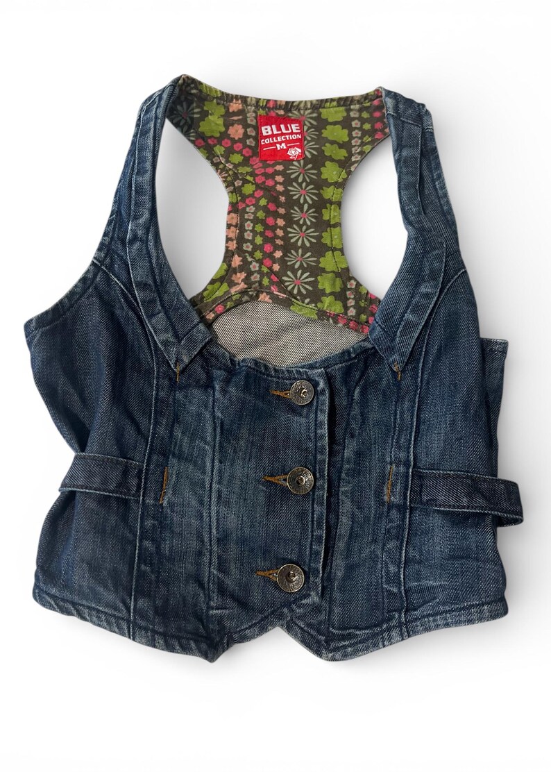 May include: A dark blue denim vest featuring a racerback design with a multi-colored floral pattern lining. The front includes three metal buttons and side adjustment tabs. A red label at the neckline reads BLUE COLLECTION M.