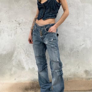 May include: A dark blue denim vest with a button-up front and a cropped hem paired with medium-wash blue denim jeans featuring a button-fly closure, distressed detailing, and a straight-leg fit that pools slightly at the bottom hem.
