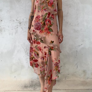 Può includere: Un abito midi color pesca tenue caratterizzato da una vivace stampa floreale nei toni del rosso, rosa e verde. Il capo presenta sottili spalline, uno scollo a V e dettagli a balze che scendono diagonalmente lungo la parte anteriore.