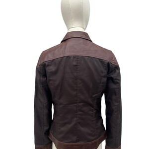 May include: A dark brown jacket with a contrasting brown leather collar and trim. The jacket is displayed on a mannequin, showcasing the back view. The jacket has a classic design with a tailored fit.
