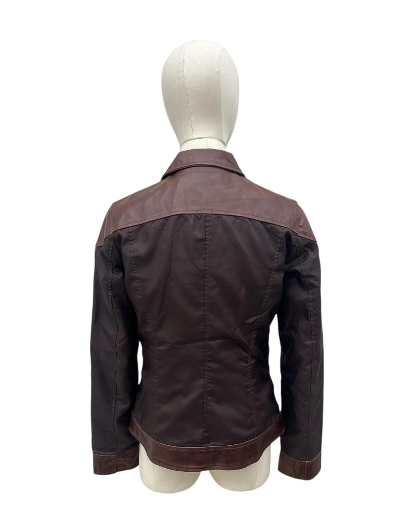 May include: A dark brown jacket with a contrasting brown leather collar and trim. The jacket is displayed on a mannequin, showcasing the back view. The jacket has a classic design with a tailored fit.