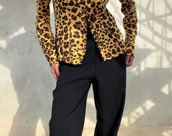 Op de afbeelding: Een button-down shirt met een luipaardprint in tinten bruin en beige, gecombineerd met een zwarte broek met wijde pijpen. De outfit toont een contrast tussen de top met patroon en de effen zwarte broek, wat een modieuze look creëert.