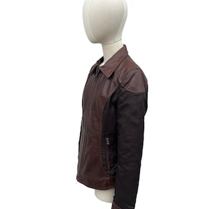 May include: A brown and black leather jacket with a collared neckline and a zipper closure. The jacket has a contrasting black panel on the sleeves and a small pocket on the chest. The jacket is displayed on a mannequin.