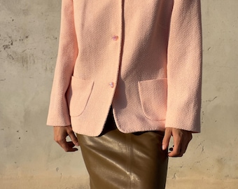 Könnte beinhalten: Ein hellrosa strukturierter Blazer mit Kragen, langen Ärmeln und drei Knöpfen auf der Vorderseite. Die Jacke verfügt über zwei aufgesetzte Taschen an der Taille und wird mit einem glatten, olivgrünen Midirock kombiniert.