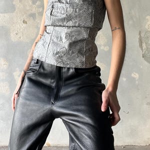 May include: A snakeskin-effect strapless top and black leather trousers. The top is light grey with a textured pattern. The trousers are high-waisted with a straight leg and lace-up detailing on the side.