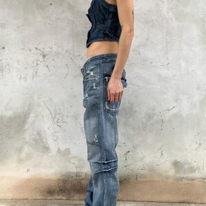 May include: A dark blue denim vest with a button-up front and a cropped hem paired with light blue distressed denim jeans featuring a low-rise waist, multiple pockets, and horizontal seam detailing along the legs in a relaxed, straight-leg fit.