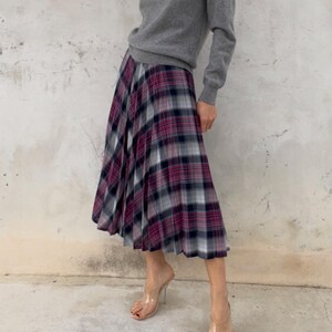 May include: A person wearing a gray V-neck sweater and a pleated plaid skirt in shades of burgundy, black, and white. The person is also wearing clear high-heeled sandals.