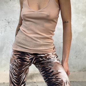 May include: A light peach-colored camisole top with thin straps and a V-neck is paired with brown and tan zebra-print pants. The pants have a flared leg. The outfit is casual and stylish.