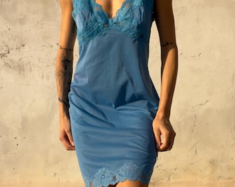 Könnte beinhalten: Ein blaues Unterkleid mit V-Ausschnitt, verziert mit floraler Spitzenborte am Oberteil und einem passenden, gebogten Spitzenabschluss am Saum. Das Kleid hat breite Träger und einen glatten, einfarbigen Rock, der über dem Knie endet.