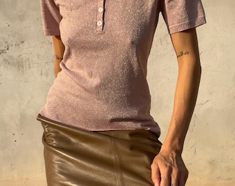 Könnte beinhalten: Ein kurzärmeliges, hellrosa Poloshirt mit dezentem metallischem Schimmer, klassischem Kragen und einer Knopfleiste mit drei Knöpfen. Das Oberteil wird mit einem glatten, olivgrünen Midirock mit gerader, figurbetonter Passform kombiniert.