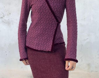 Könnte beinhalten: Eine pflaumenfarbene Wickeljacke mit strukturiertem Blumenmuster und dunklem Samtbesatz am V-Ausschnitt und an den Ärmelbündchen, kombiniert mit einem passenden pflaumenfarbenen Strick-Midirock. Das Set hat lange Ärmel und eine körpernahe Passform.