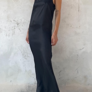 May include: A floor-length black slip dress with a V-neckline and thin spaghetti straps. The garment is made of a smooth, satin-like fabric that drapes along the body, featuring a simple, unadorned design that reaches down to the floor.