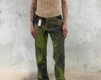 Könnte beinhalten: Ein beiges Korsett-Top mit eckigem Ausschnitt und dünnen Trägern, kombiniert mit einer geraden Jeans mit grün-schwarzem Blattmuster, verwaschener Optik und einem kleinen weißen rechteckigen Etikett am Hosenbund.