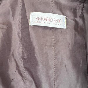 May include: Close-up of a brown garment's interior, showcasing a stitched, quilted texture. A rectangular label with the text "ANTONELLO SERIO MADE IN ITALY" is visible. The fabric appears to be a soft, possibly leather-like material.