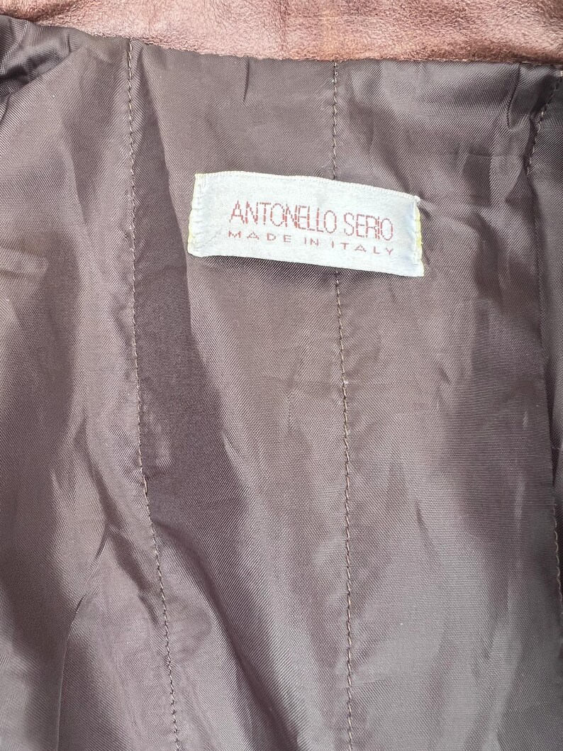 May include: Close-up of a brown garment's interior, showcasing a stitched, quilted texture. A rectangular label with the text "ANTONELLO SERIO MADE IN ITALY" is visible. The fabric appears to be a soft, possibly leather-like material.