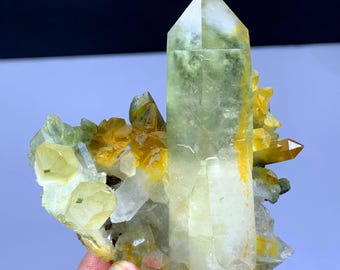 May include: A cluster of clear quartz crystals with yellow and green inclusions. The crystals are arranged in a cluster, with the largest crystal in the center. The crystals are translucent and have a glassy luster.