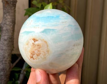 May include: A spherical gemstone with a marbled appearance. The orb features bands of light blue and white, with a prominent patch of tan and brown. The polished surface reflects light, creating a captivating display. This decorative sphere is a unique home decor item.