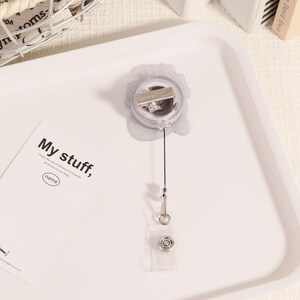 May include: A clear retractable badge holder with a silver clip and a black cord. The badge holder has a clear plastic snap closure. A white card with the text "My stuff," is also in the image.