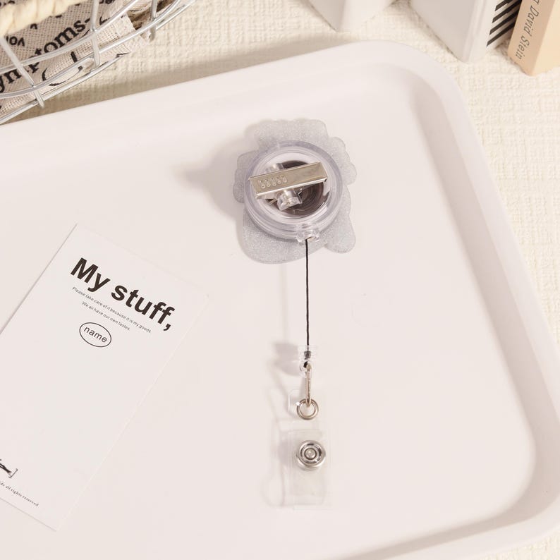 May include: A clear retractable badge holder with a silver clip and a black cord. The badge holder has a clear plastic snap closure. A white card with the text "My stuff," is also in the image.