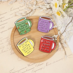 Könnte beinhalten: Vier Emaille-Tassen-Anstecknadeln in Grün, Lila, Gelb und Rot, jede mit einem anderen Zitat. Die grüne Tasse sagt: "You can't pour from an empty cup." Die lila Tasse sagt: "May your coffee and your pelvic floor be strong." Die gelbe Tasse sagt: "At this point I'm just living from one cup of tea to the next..." Die rote Tasse sagt: "It's time to bring out the big mug."