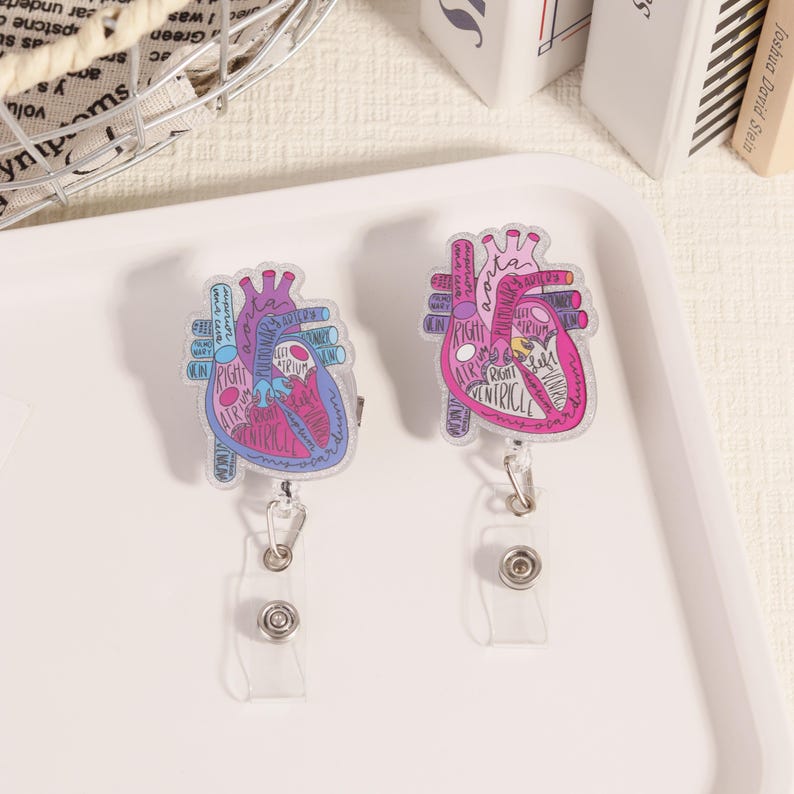 May include: Two heart-shaped badge reels with anatomical diagrams. One is blue and the other is pink, both with labels like "Right Atrium" and "Ventricle." Each reel has a clear plastic strap and a metal clip.