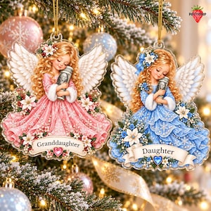 May include: Two flat Christmas ornaments featuring blonde angels with wings, one in a pink dress labeled Granddaughter and one in a blue dress labeled Daughter. Both angels hold a rolled-up one-hundred-dollar bill. Each ornament is decorated with flowers.