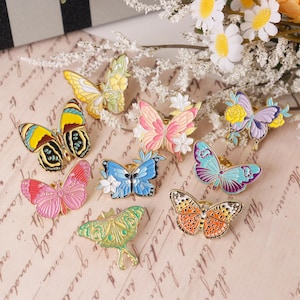 Pode incluir: Conjunto de broches de borboleta de esmalte colorido com designs florais e geométricos. Os broches estão dispostos sobre um fundo de papel com aparência vintage.