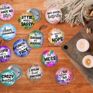 Peut inclure: Plusieurs boutons ronds colorés avec des phrases humoristiques telles que "Hot Mess Express" et "Too Glam To Even Care". Les boutons ont une épingle et sont disposés sur une surface en bois.