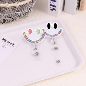 Peut inclure: Deux enrouleurs de badge blancs avec un motif de grenouille. L'un porte l'inscription "COSAS PARA RECORDAR" et l'autre "BE KIND TO YOUR MIND". Les deux ont une sangle en plastique transparent et un clip en métal.