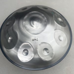 May include: A silver handpan with a paw print logo in the center. The handpan has eight notes and a black rim.