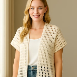 Könnte beinhalten: Cremefarbene Strickjacke mit offenem Vorderteil und kurzen Ärmeln. Die Strickjacke hat ein gewebtes, offen gestricktes Design. Die Person trägt ein weißes Tanktop und blaue Jeans. Die Strickjacke ist ein vielseitiges Kleidungsstück.