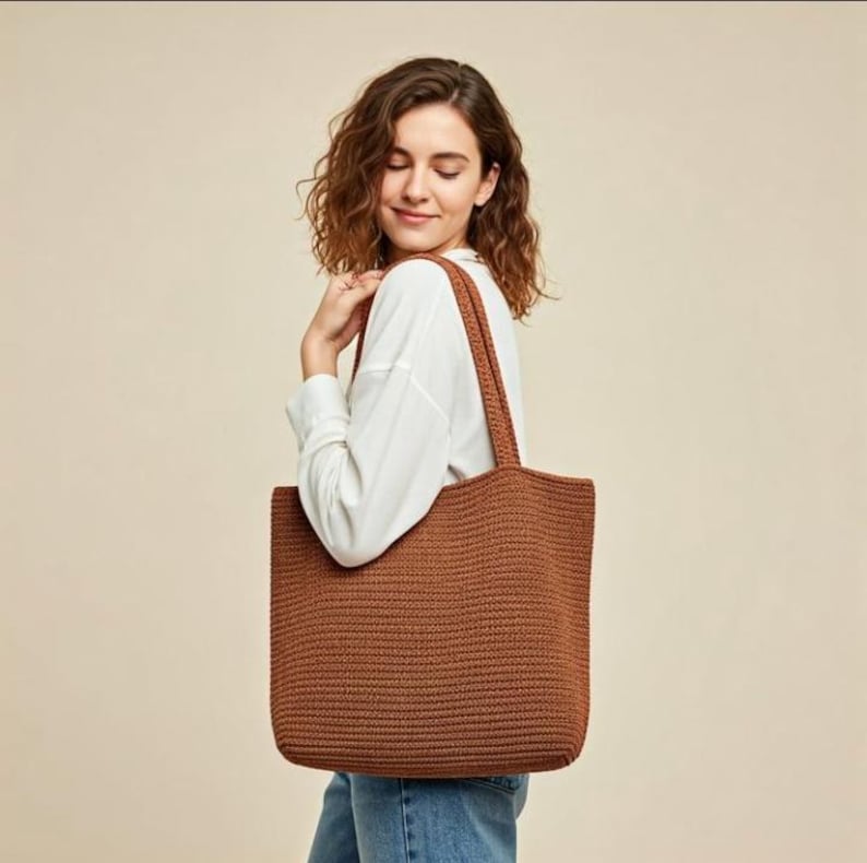 Pu&ograve; includere: Una borsa tote marrone all'uncinetto con manici lunghi. La borsa &egrave; rettangolare con un'ampia apertura e una superficie strutturata. La borsa viene portata a spalla.