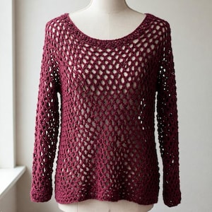 May include: A maroon crocheted sweater with a loose, open-weave pattern. The sweater has long sleeves and a round neckline.