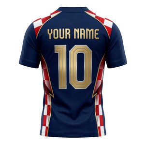 May include: Navy blue short-sleeve jersey with gold lettering and numbers. The jersey features the text "YOUR NAME" above the number "10". Red and white checkered pattern accents the shoulders and sides. A sports-themed apparel item.