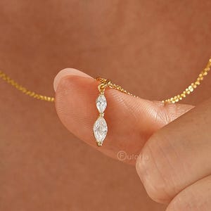 May include: A gold chain necklace featuring a vertical pendant with two marquise-cut clear stones set in gold. The pendant consists of a smaller marquise stone positioned above a larger marquise stone, both held by gold prongs on a delicate chain.