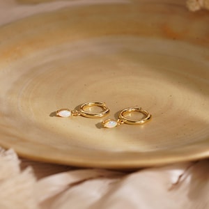 May include: A pair of gold hoop earrings, each featuring a small, dangling marquise-cut opal gemstone. The earrings have a polished metallic finish and a secure hinged closure mechanism, showcasing a simple and refined design for everyday wear.