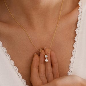 May include: A delicate gold necklace featuring two diamond pendants: a square-cut stone above a pear-shaped stone. The necklace is displayed against a white background. The jewelry is from the brand "Fuloria".