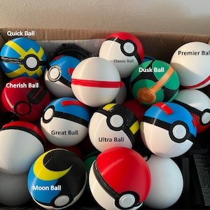 May include: A collection of spherical plastic toys resembling various types of Poké Balls, including Quick Ball, Cherish Ball, Great Ball, Moon Ball, Classic Ball, Ultra Ball, Dusk Ball, and Premier Ball, all contained within a cardboard box.