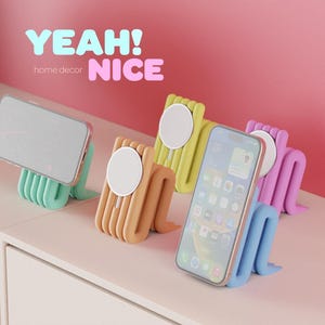 Könnte beinhalten: Bunte Handyhalterungen in Mintgrün, Beige, Gelb und Lila, jeweils mit einem Smartphone. Die Halterungen haben ein einzigartiges, wellenförmiges Design. Der Text oben lautet "YEAH! NICE" und "home decor".