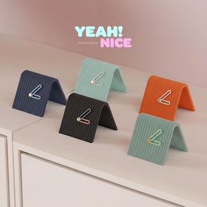 Könnte beinhalten: Fünf farbenfrohe, gewölbte Schreibtisch-Organizer in Marineblau, Schwarz, Meergrün, Orange und Hellgrün. Jeder Organizer hat einen akzentartigen Papierclip. Der Text "YEAH! NICE home decor" ist im Hintergrund sichtbar.